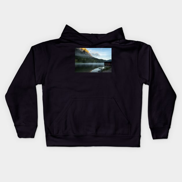 Misty Lake Portrait wide angle with boathouse. Amazing shot of a wooden house in the Ferchensee lake in Bavaria, Germany, in front of a mountain belonging to the Alps. Scenic foggy morning scenery at sunrise. Kids Hoodie by EviRadauscher